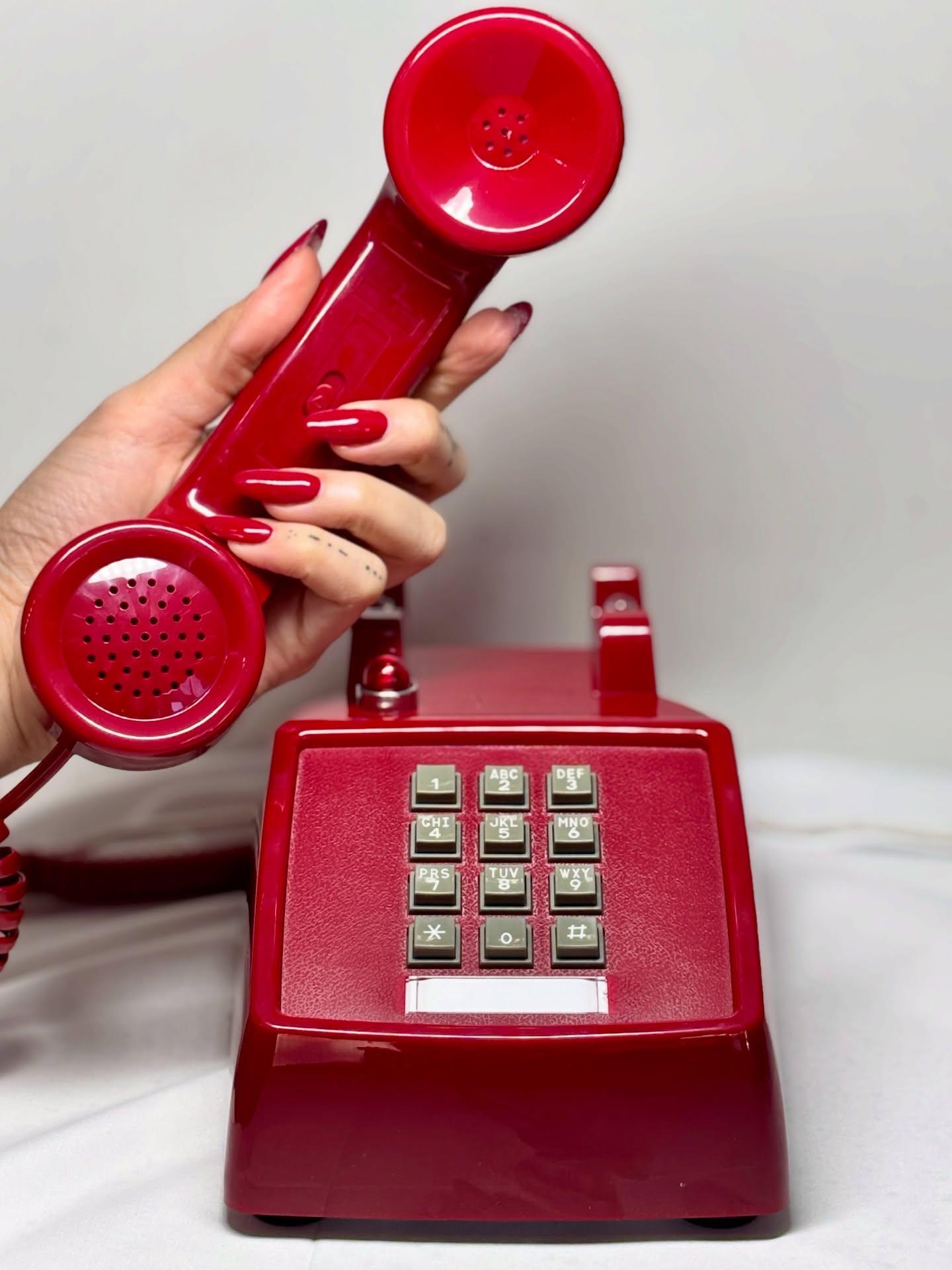 Red manicure holding a vintage red telephone at The Beauty Shoppe